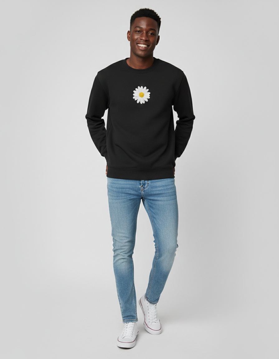 Man wearing a black sweatshirt with a white daisy design and blue jeans on a gray background