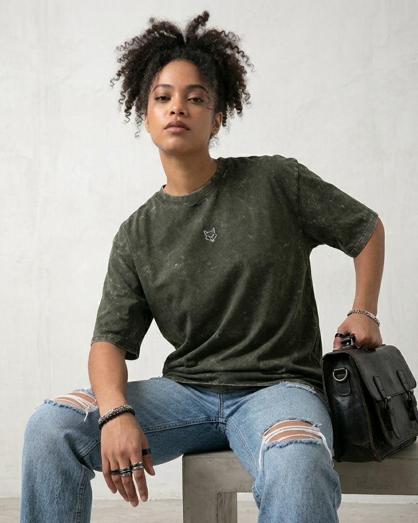 Person wearing a green t-shirt and ripped jeans sitting on a bench.